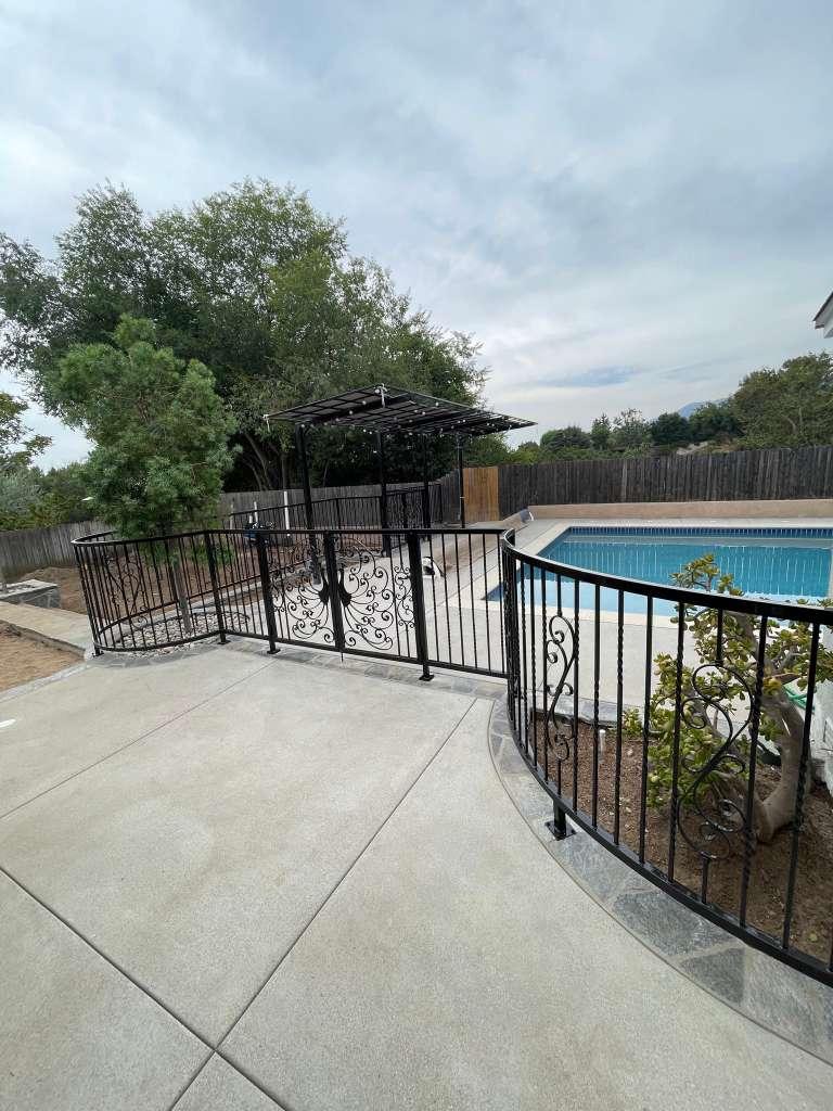 Decorative black metal safety railing installed around a residential pool and patio area