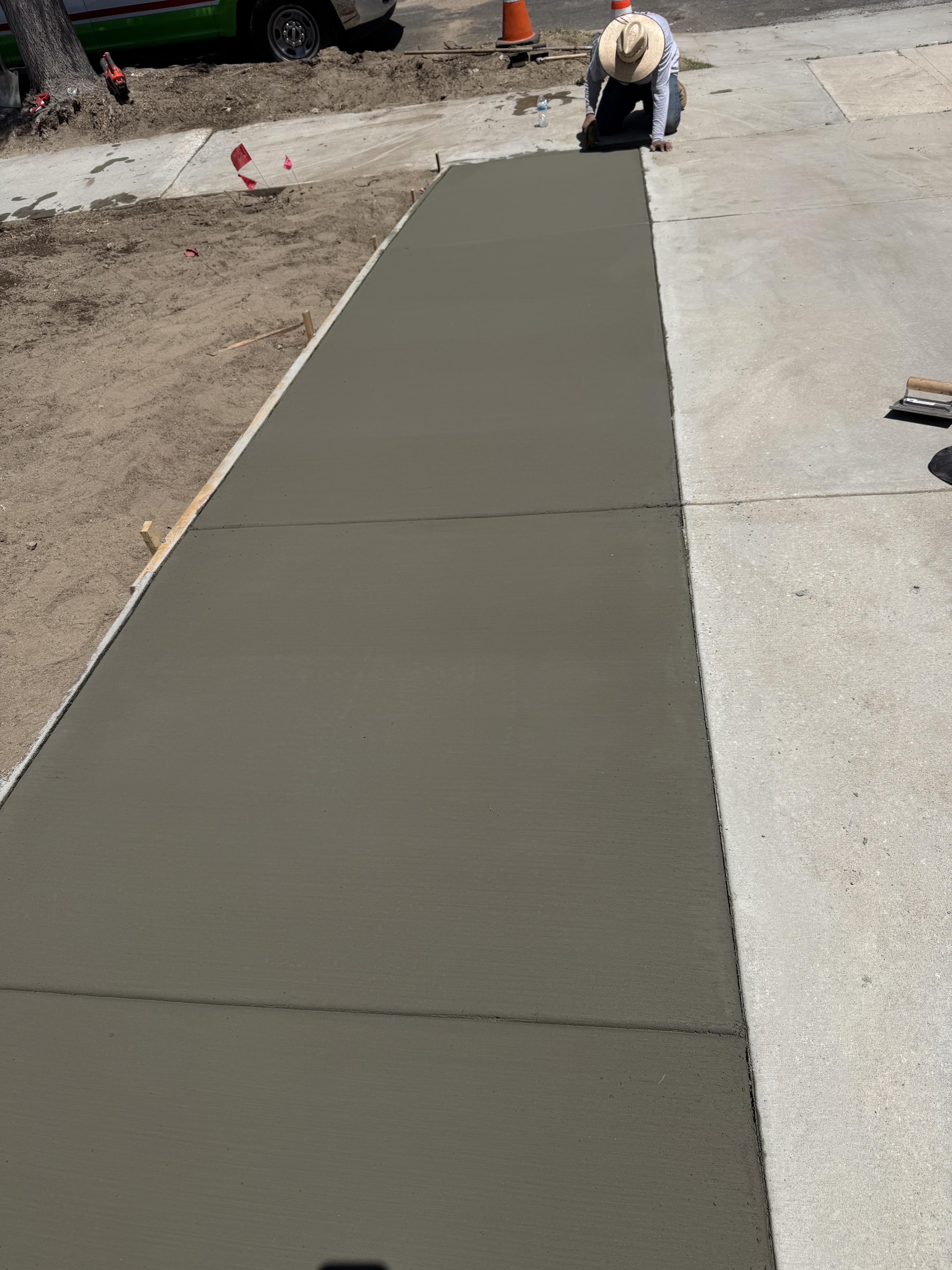 Worker finishing a newly poured concrete walkway beside an existing residential driveway