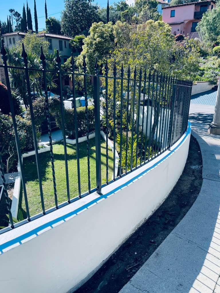 Custom black wrought iron fence with spear-top pickets installed along a curved stucco wall