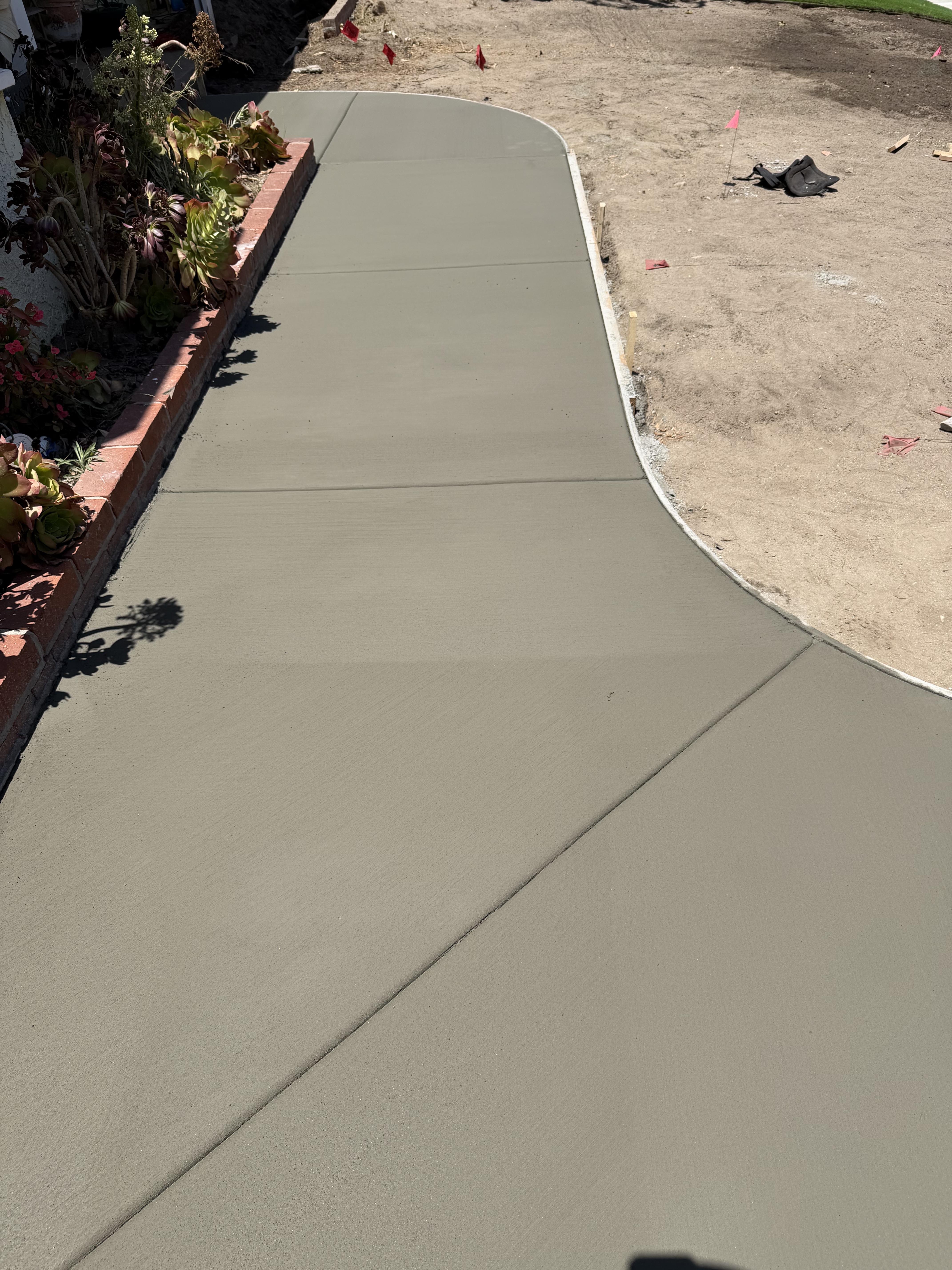 Newly poured curved concrete walkway running alongside a brick planter in a residential yard