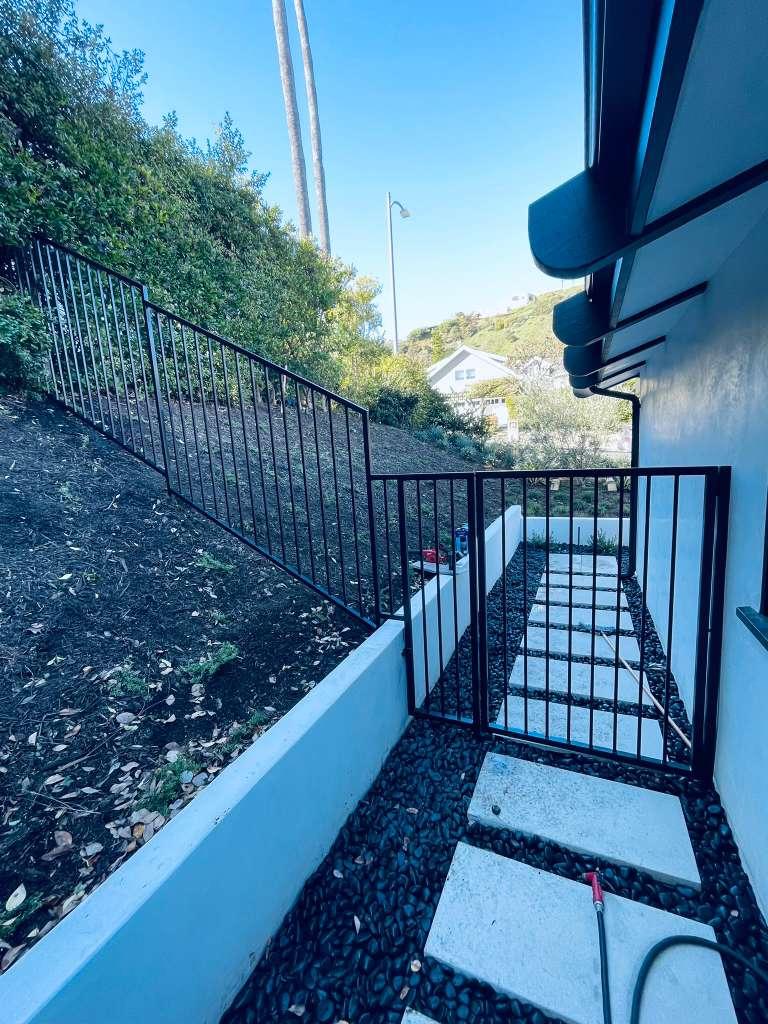 Black metal hillside railing and matching pedestrian gate installed beside a residential walkway