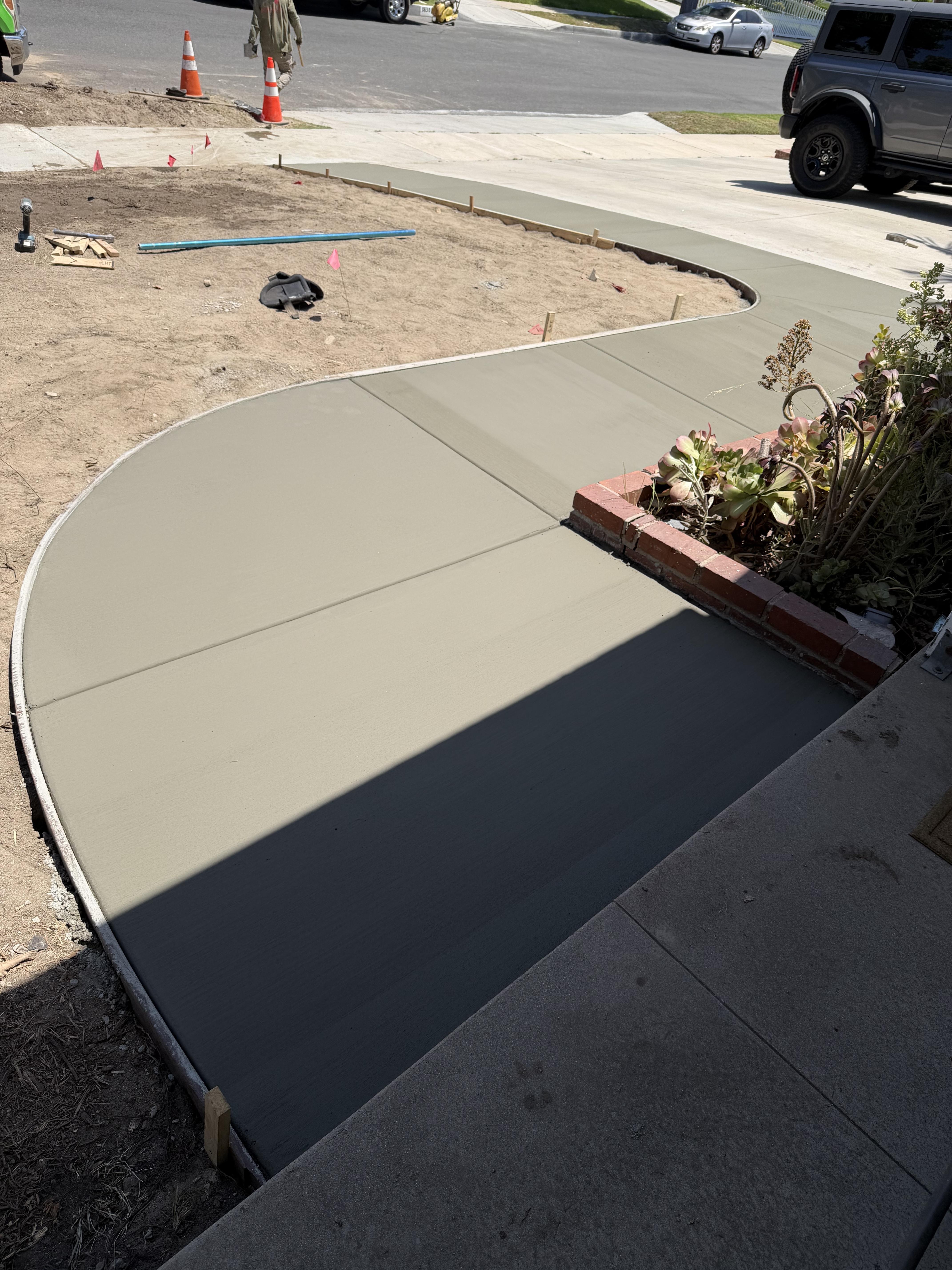 Fresh concrete walkway with smooth curved edges connecting a residential yard to the driveway