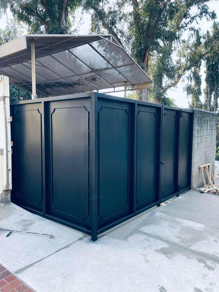 Black metal privacy enclosure with decorative recessed panels built beside a masonry wall