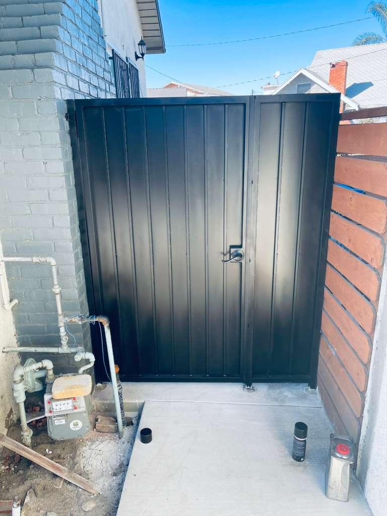 Solid black metal pedestrian gate with vertical panels and locking hardware between residential walls